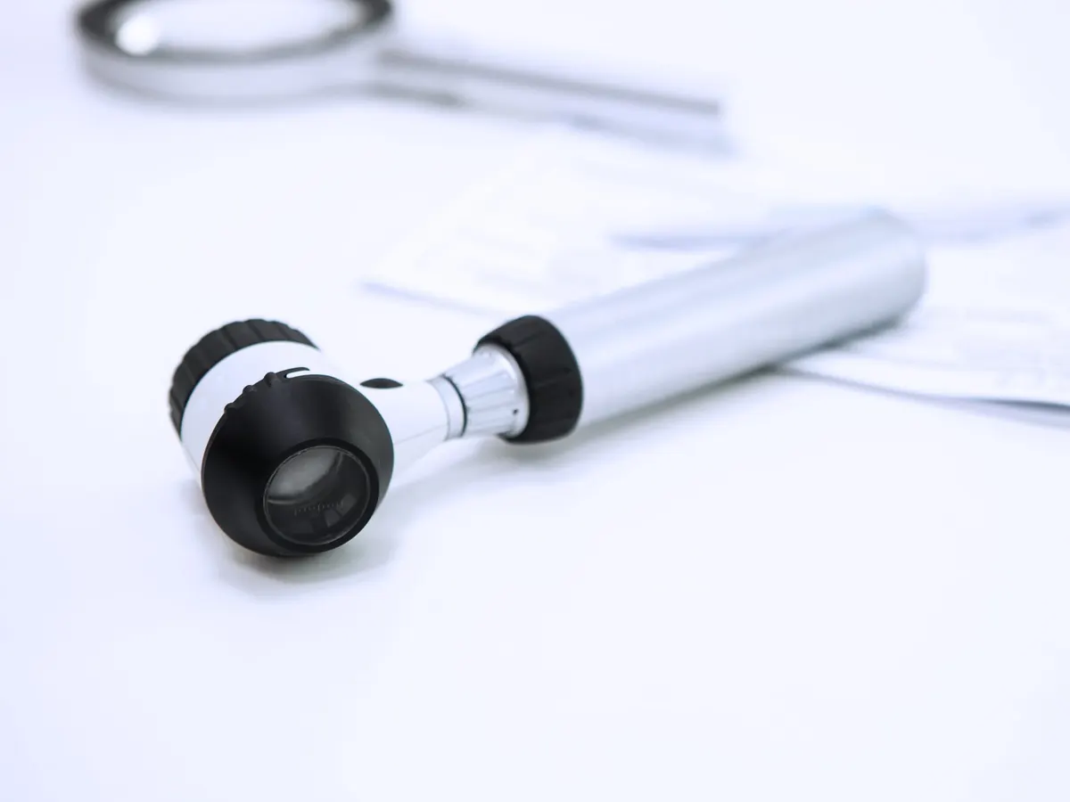 A handheld dermatoscope lying on a white clinic table beside paperwork — a stock picture