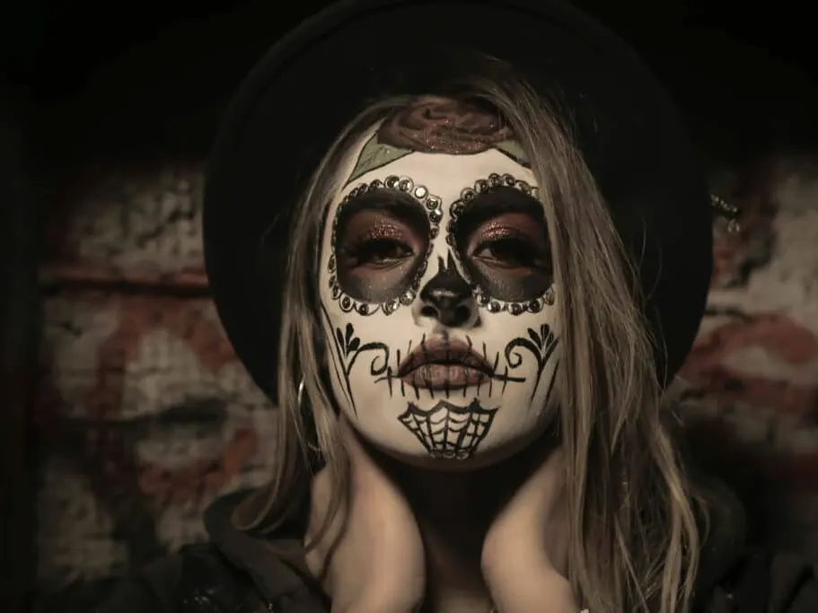 Woman in a black hat wearing skull-style Halloween face paint