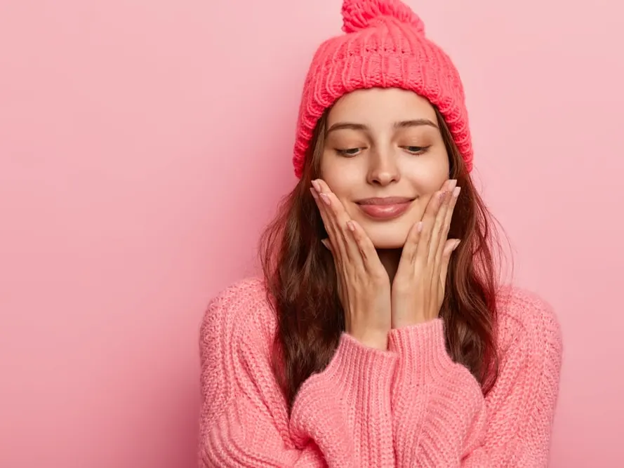 Smiling woman in a pink knit hat and sweater resting her face in her hands