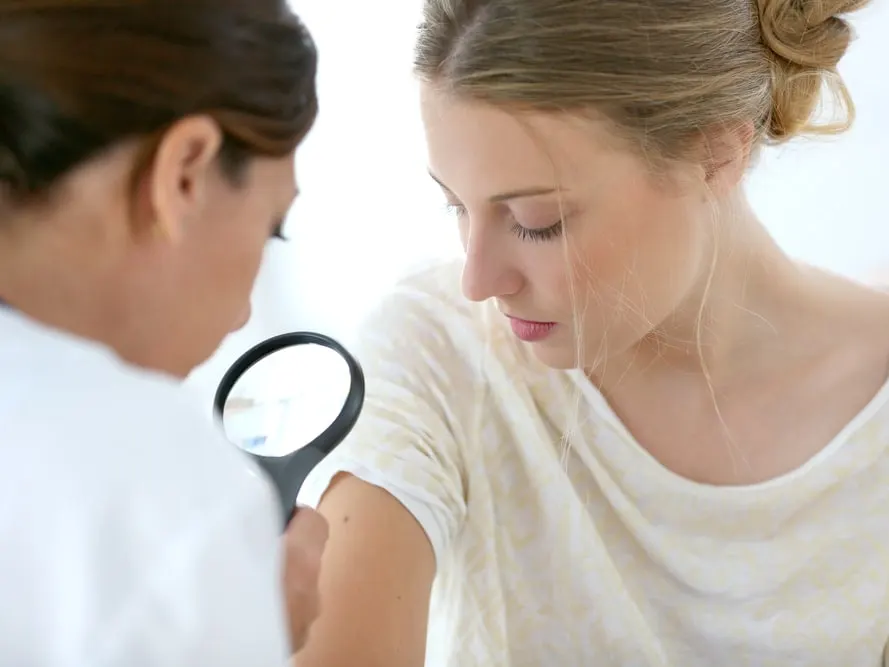 Clinician examining a young woman’s arm with a magnifying glass