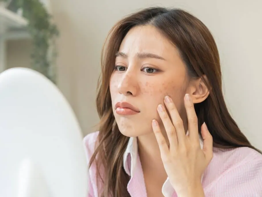 A woman looking in the mirror for signs of skin damage
