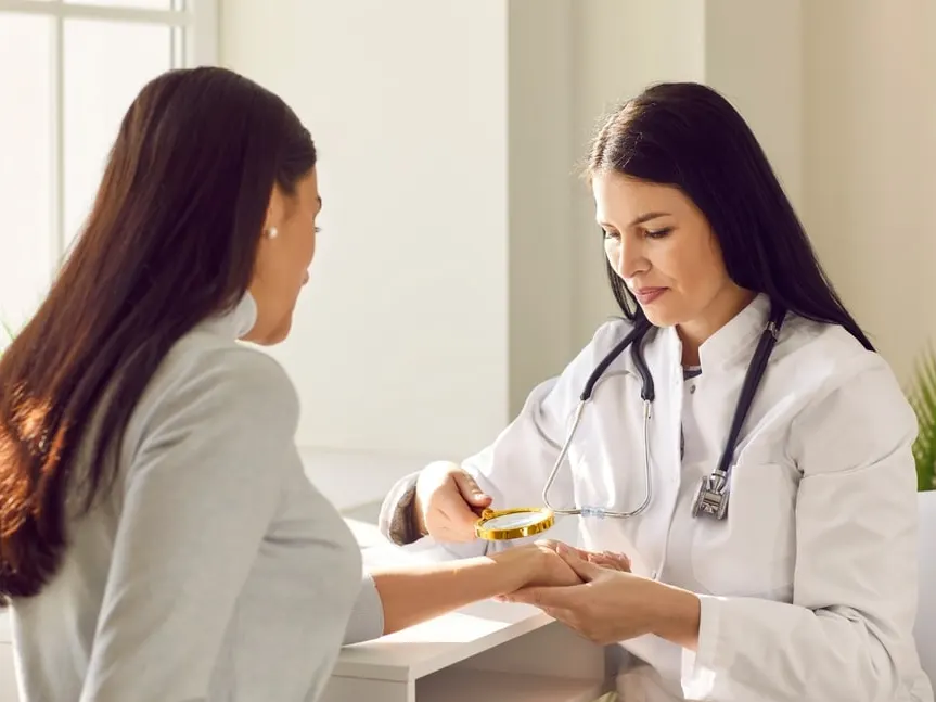 Dermatologist examining patient's wrist with magnifying class.