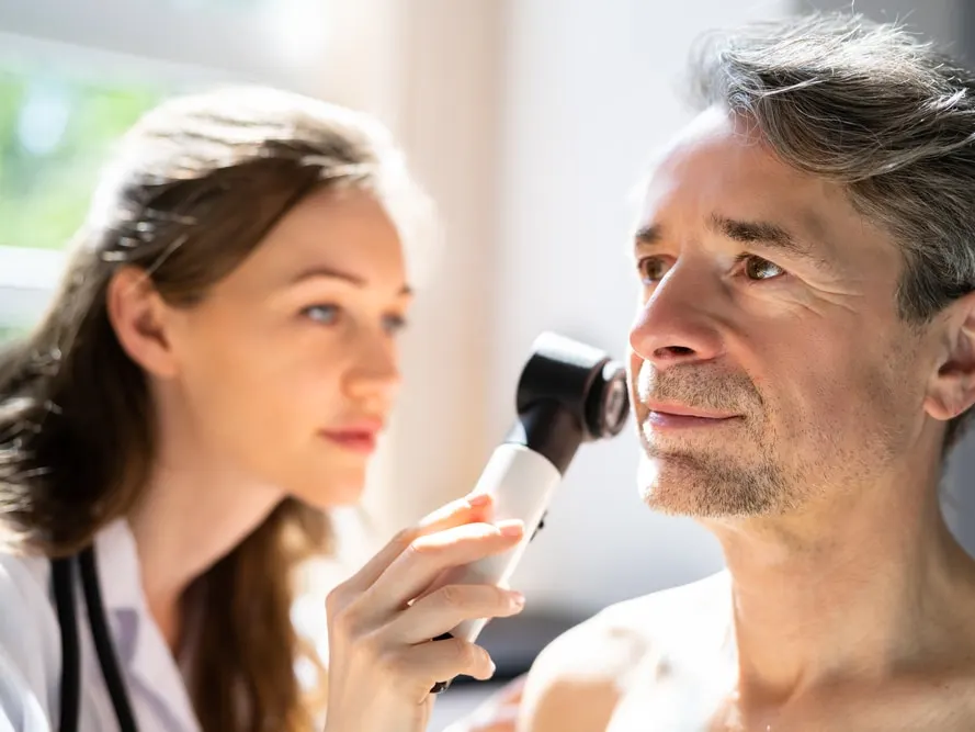 Dermatologist examines a patient’s face with a dermatoscope during a skin cancer screening for possible melanoma signs.