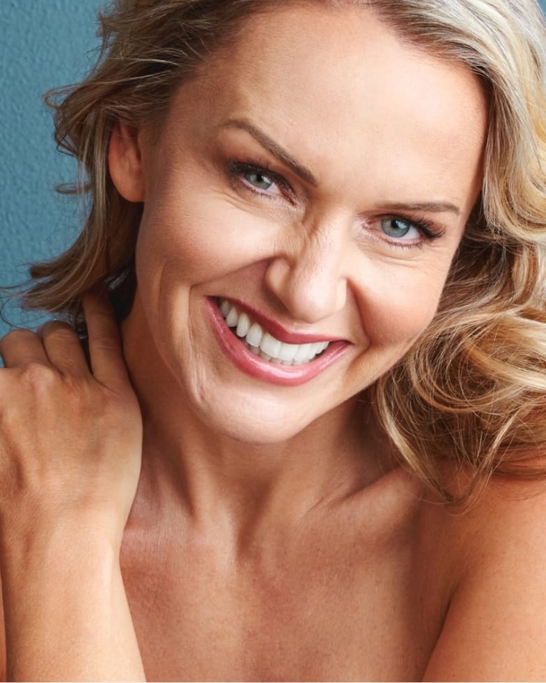 A smiling woman with wavy blonde hair against a teal wall