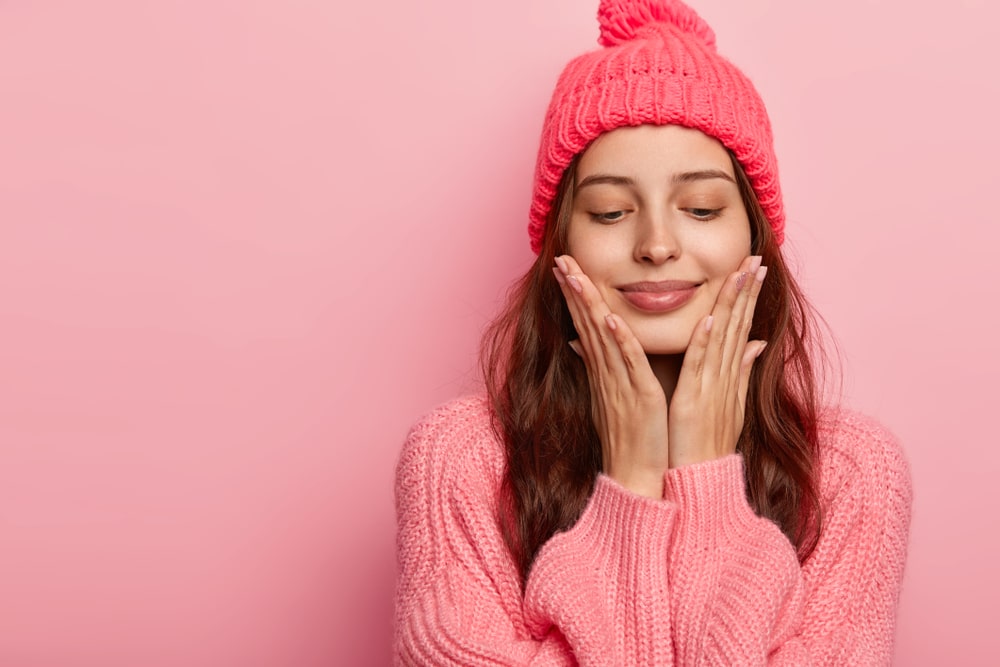Smiling woman in a pink knit hat and sweater resting her face in her hands