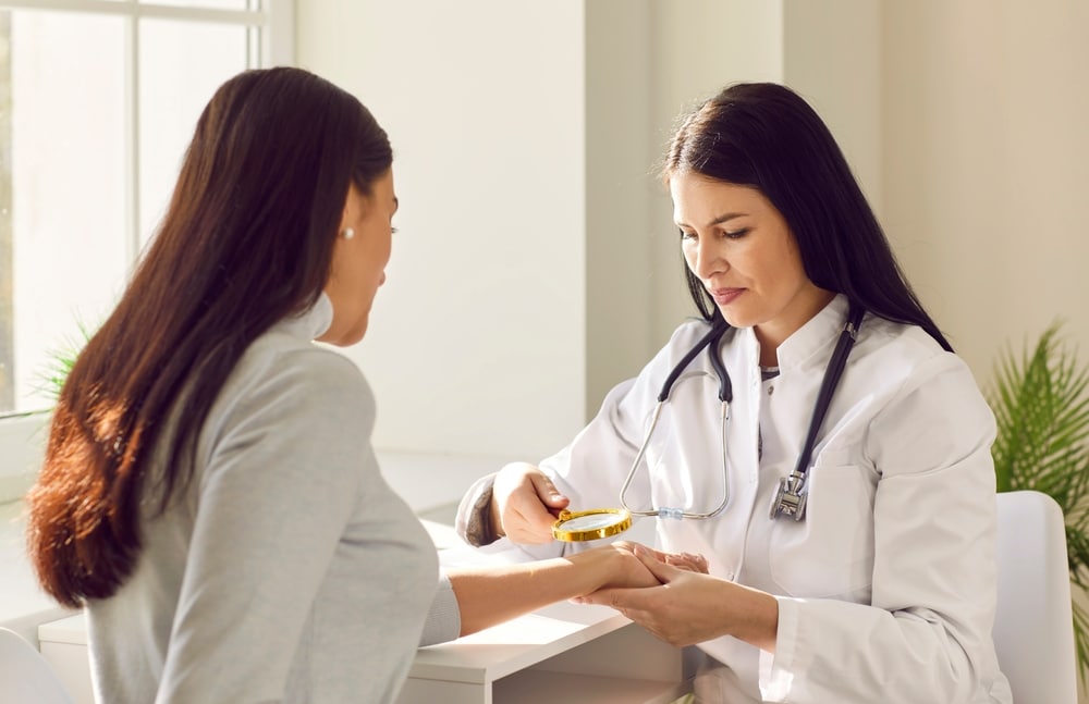 Dermatologist examining patient's wrist with magnifying class.